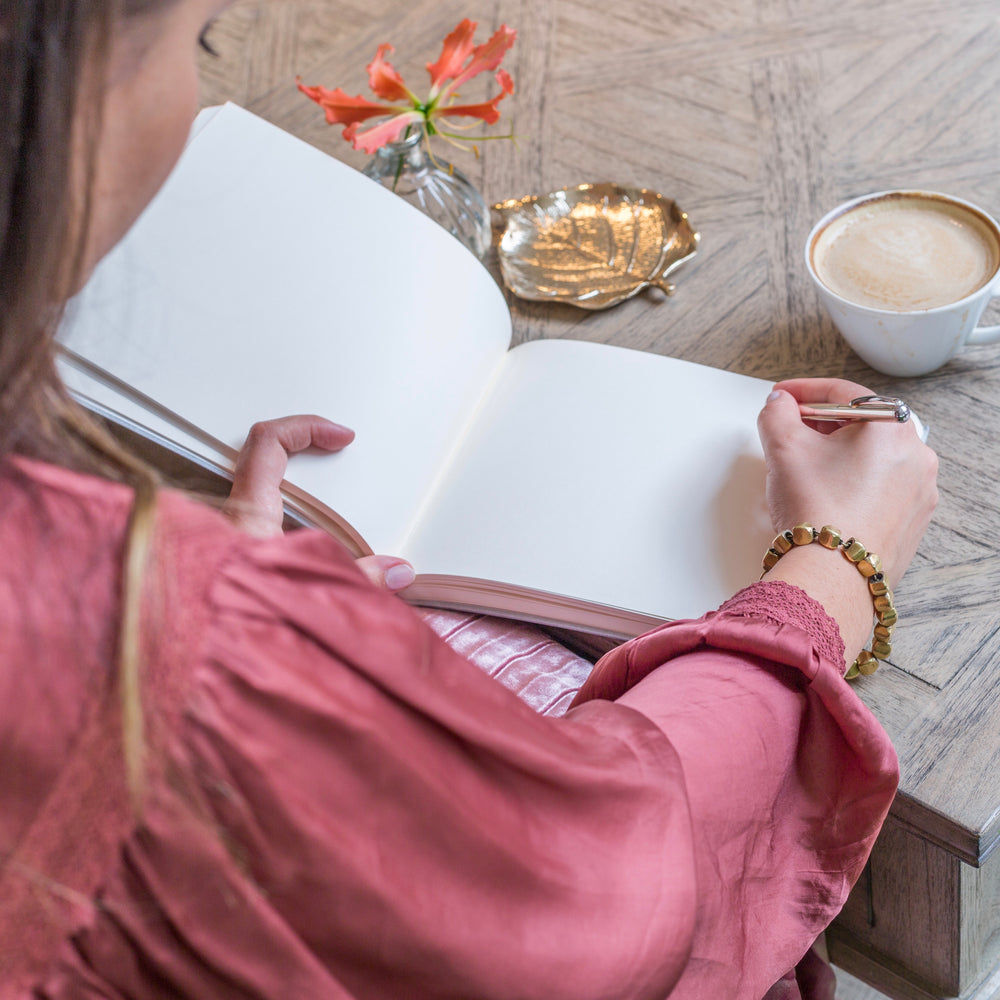 a retirement book lies open on the table and you can see the plain pages inside. A woman is poised to write a message in the retirement book