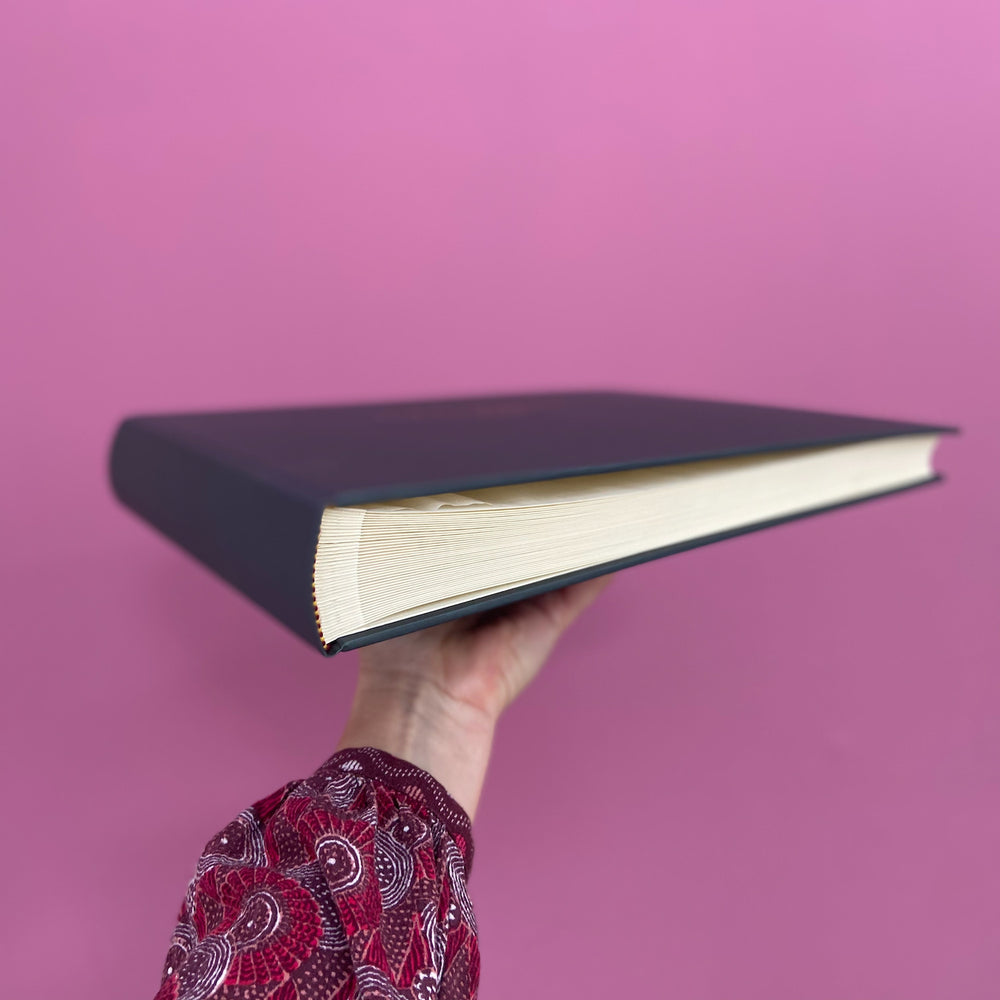 
                      
                        The condolence book is being held up against a pink background so you can see the pages and the traditional binding.
                      
                    