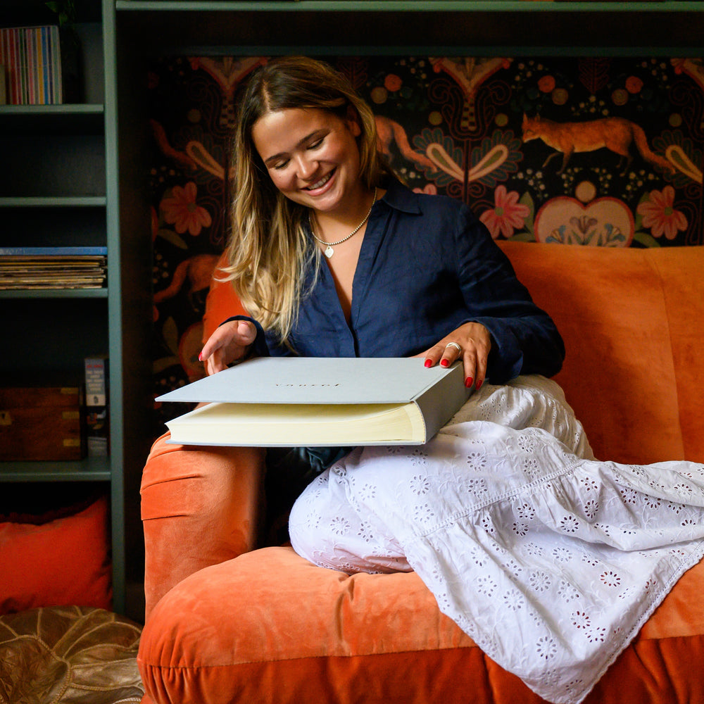 
                      
                        Lady curled up on an orange sofa about to start looking through a new baby album
                      
                    