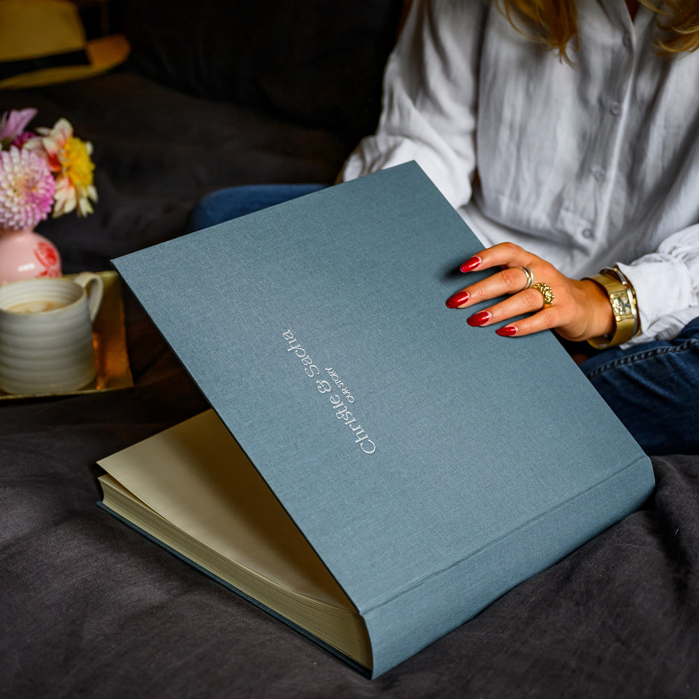 a lady sitting cross legged on a bed about to look through a gorgeous photo album