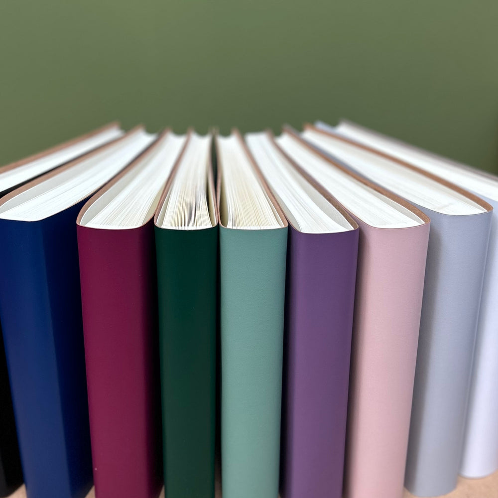 
                      
                        eight wedding guest books are standing up so you can see the colours and the traditional way in which they have been bound
                      
                    