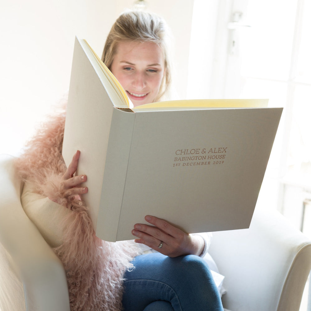 A lady sitting in a large white armchair flicking through and ivory photo album