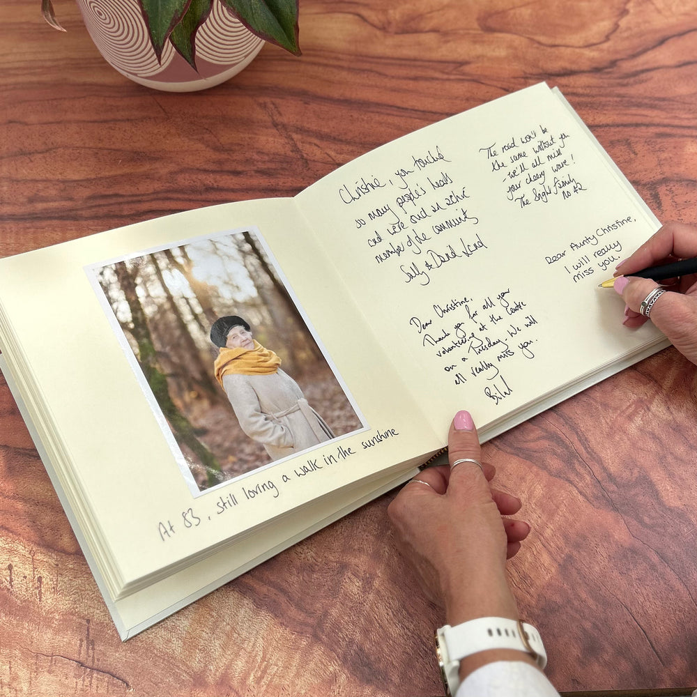 
                      
                        A condolence book lies open on a table. It has a picture of an elderly woman in it and some handwritten messages of condolence.
                      
                    