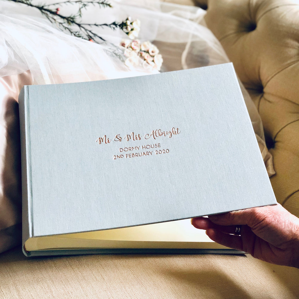 
                      
                        There is a large landscape linen wedding guest book. It has been personalised with Mr and Mrs details, the location of their wedding and it has also been dated. 
                      
                    