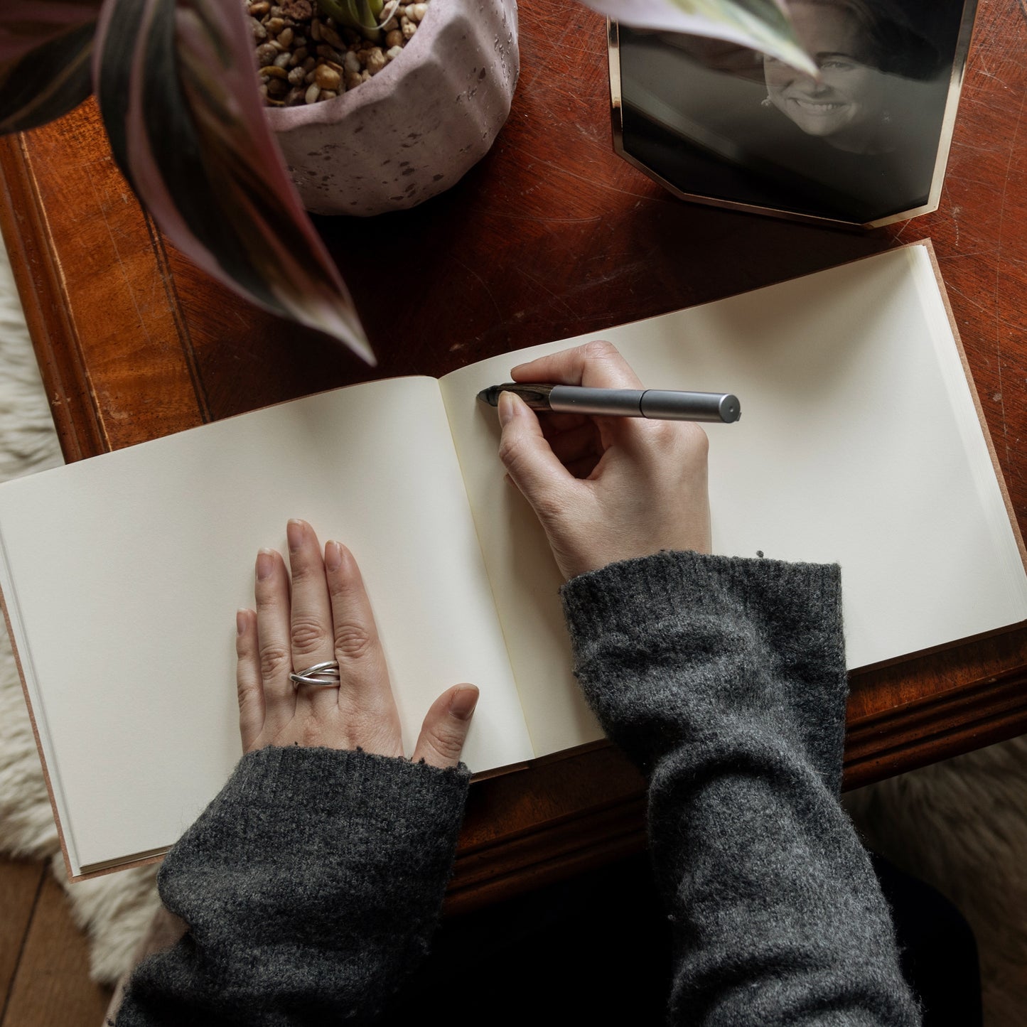 A large condolence book lies open on a wooden table and a woman in a grey jumper is poised with a pen and about to write a message inside it.