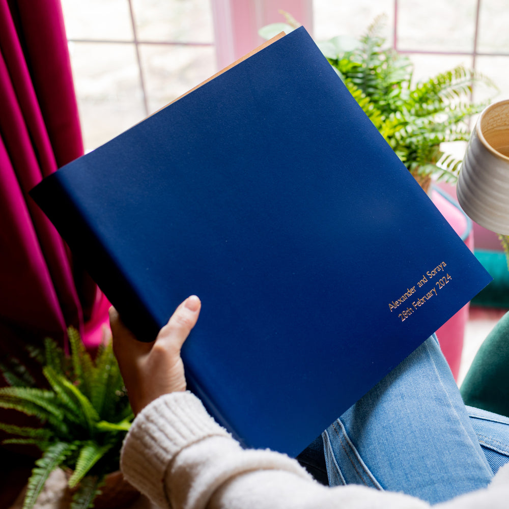 A girl is sitting in a chair holding a large leather photo album in her hands. It has also been personalised on the bottom hand right corner. 