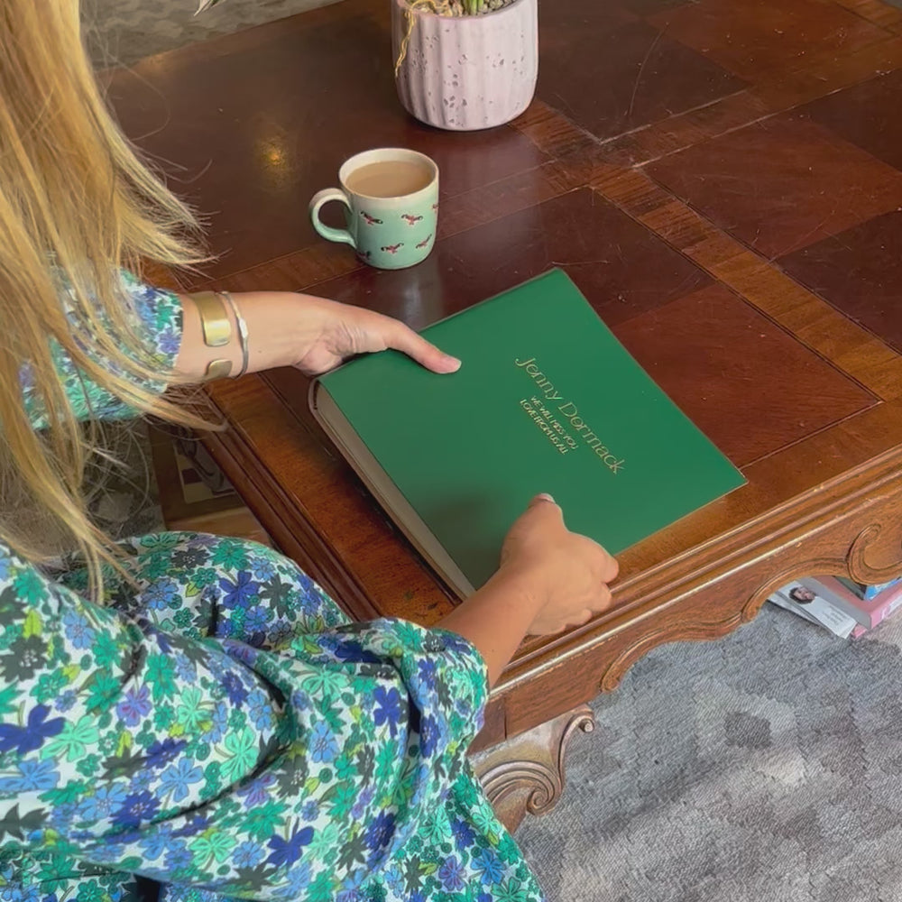 a girl picks up the condolence book, opens the first page of the condolence book and then puts it down again. The condolence book has been personalised with gold writing