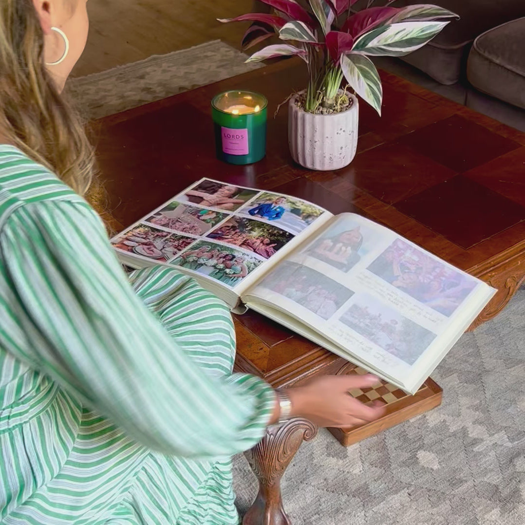 a young woman flips through a large photo album. She turns over the glassine interleaf to look at both pages. The album is filled with people celebrating 