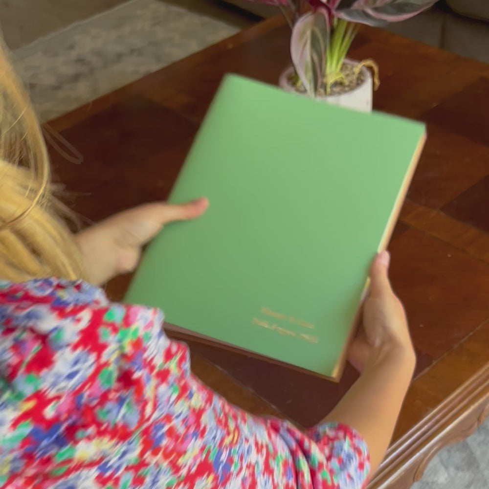 
                      
                        Load and play video in Gallery viewer, a video of a young woman flicking through a green A4 photo album that has been personalised on the front. She places it on a coffee table with a plant on it
                      
                    