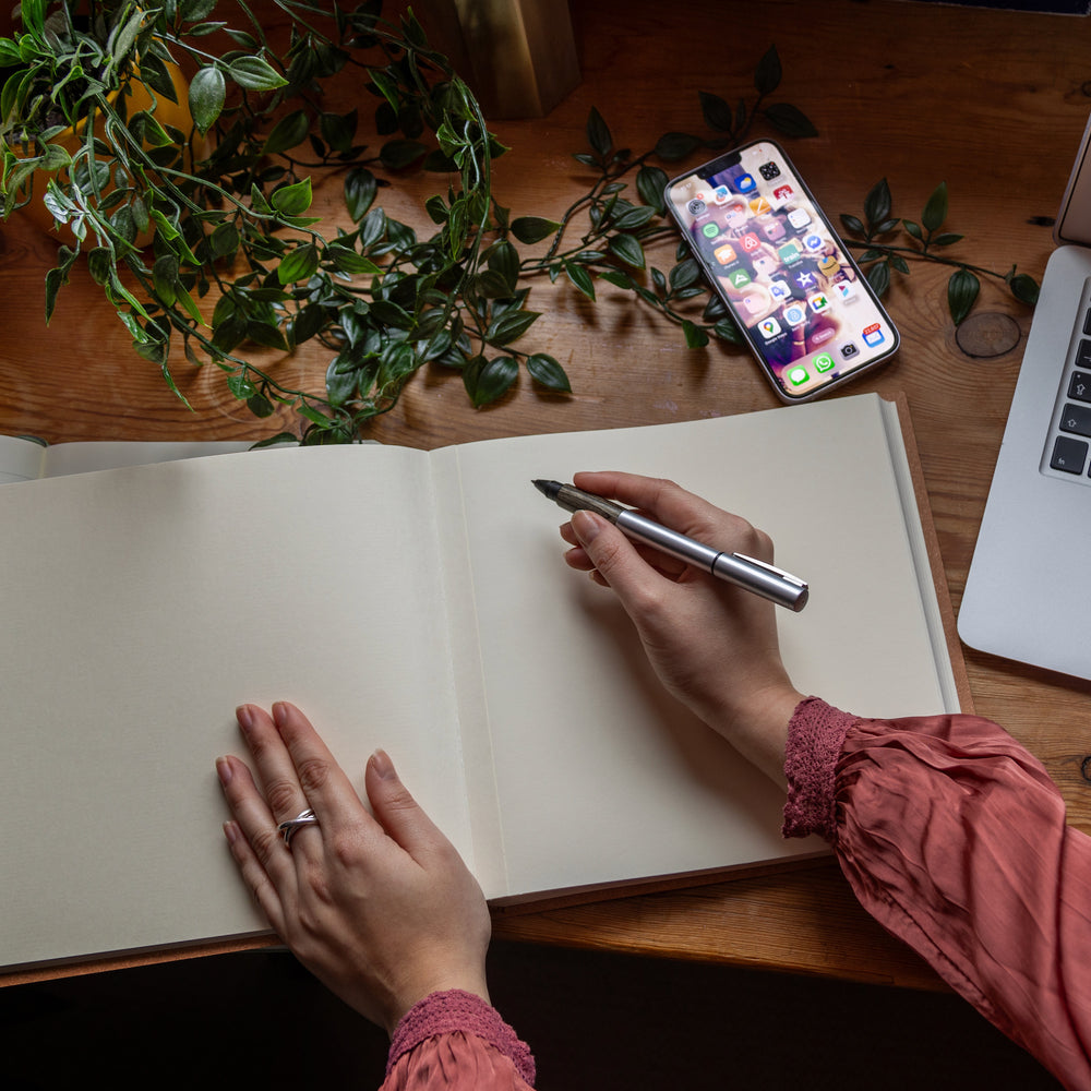 A retirement book lies open on a wooden work desk and you can see a woman with a pen about to write a message inside.