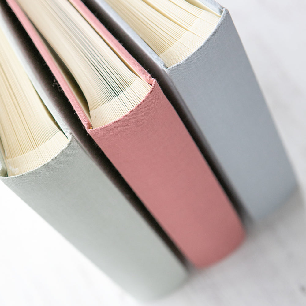 
                      
                        There are three linen albums stacked in a row. You can see three of the different colours available. Both the bind and the interior of the book is visible. 
                      
                    