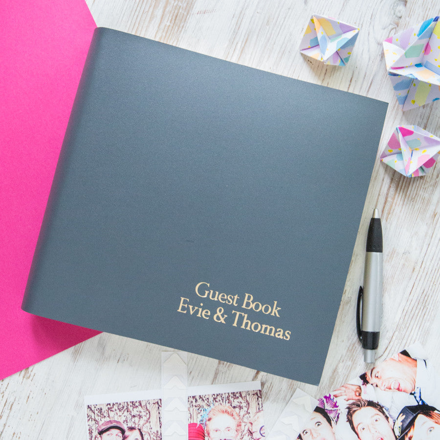 This large leather guest book had been personalised in the bottom right hand corner. It is on a wooden table, there are photographs and a pen by the side of the book.