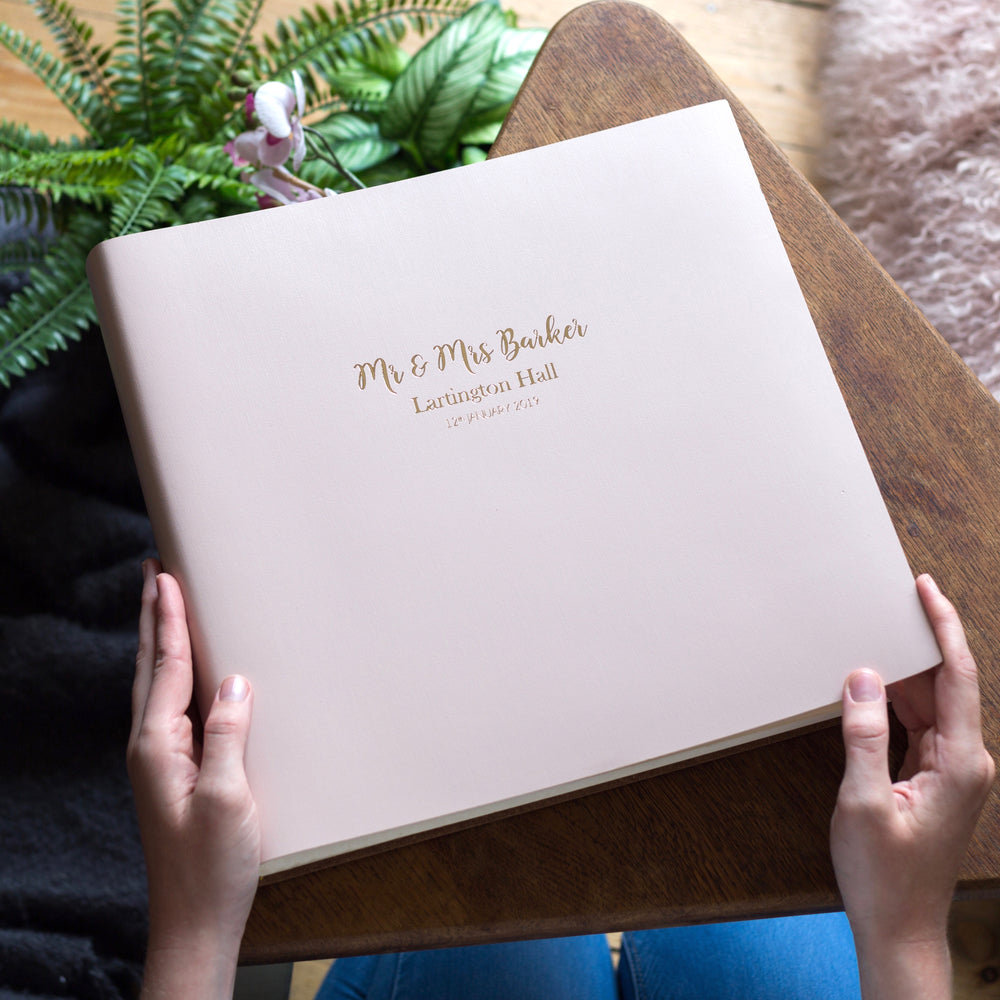 There is a woman holding a pink large leather photo album. It has been personalised with gold hot foil.